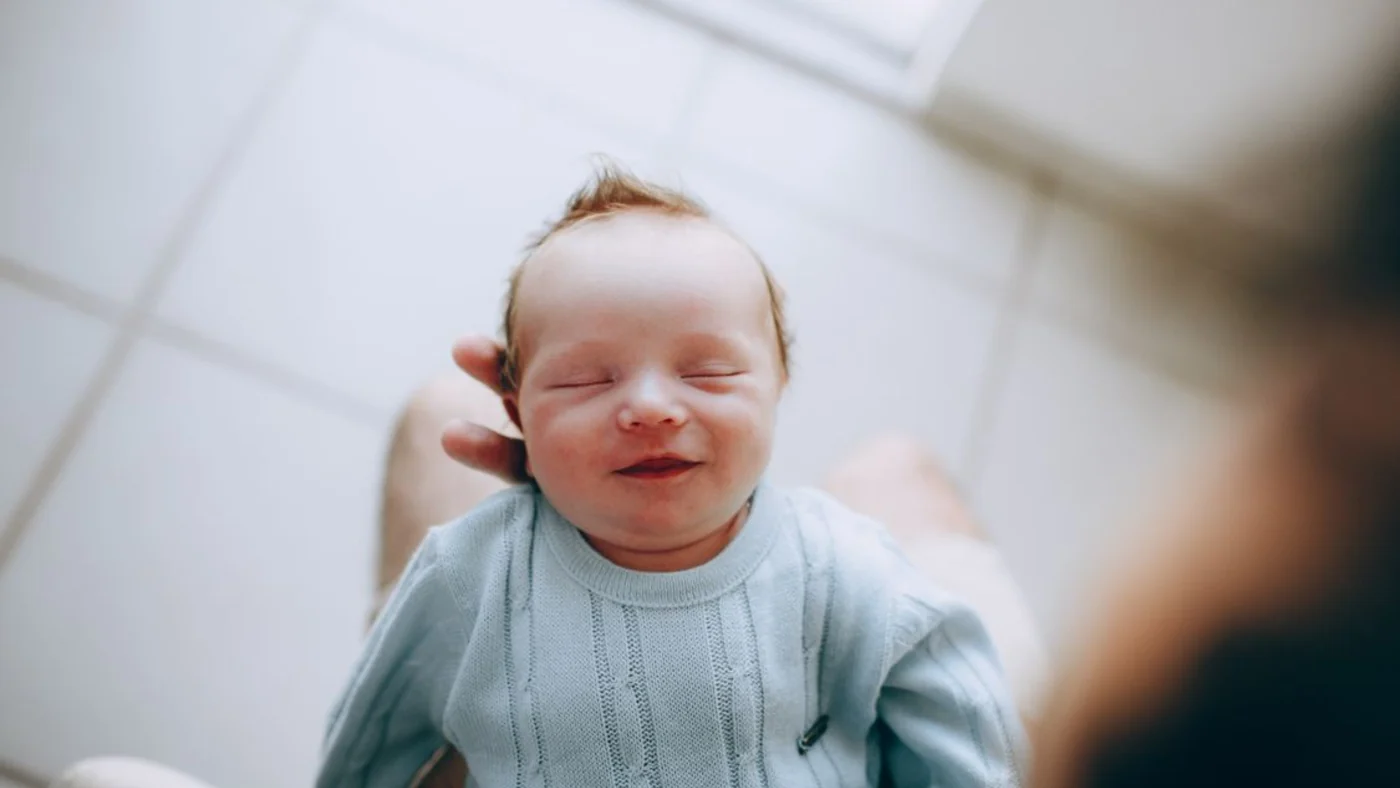Close-up of a calm baby with a small smile in a caregiver's arms.