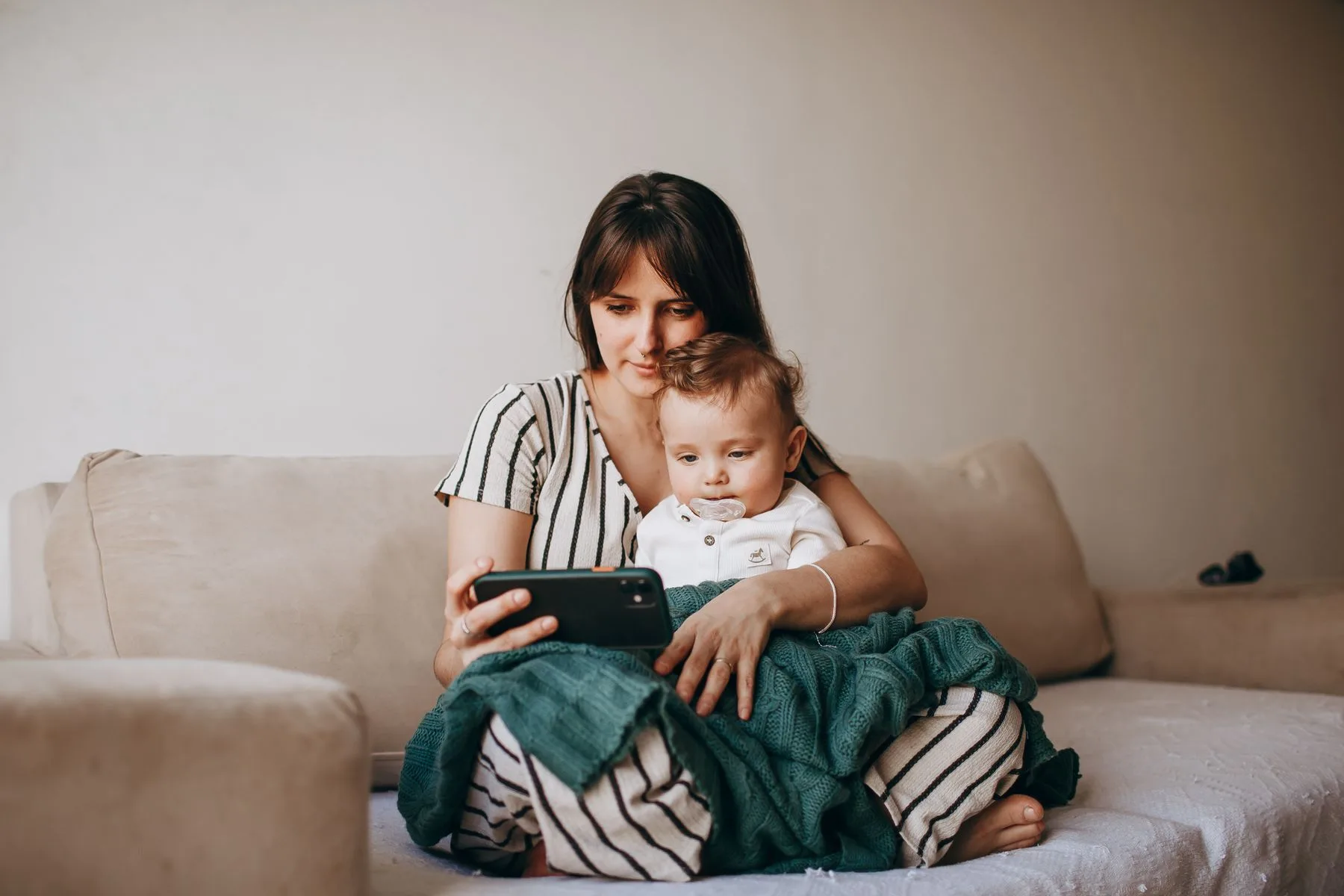 Mother holding her baby looks at a smartphone during a calm caregiving moment.